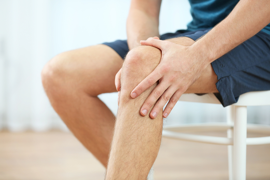Young man suffering from knee pain at home, closeup