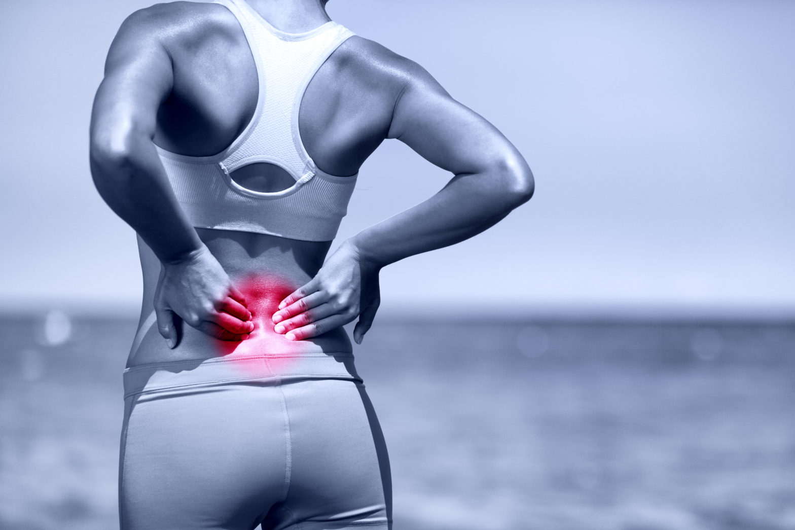 Back pain. Athletic running woman with back injury in sportswear rubbing touching lower back muscles standing on road outside.